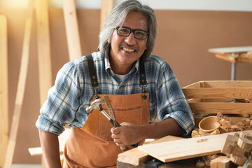 Asian senior carpenters working in the workshop, smiling and looking at camera, concept of  works in a carpentry shop