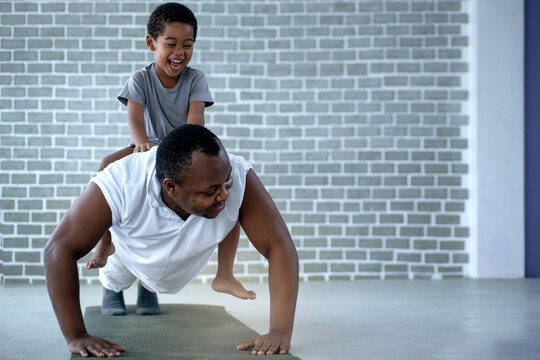 African dad and son exercise on floor at home, man push up from the floor with the boy on his back, father's day