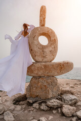Woman sea stone. A woman stands on a stone sculpture made of large stones. She is dressed in a...