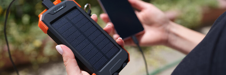 Obraz na płótnie Canvas Hands holding solar power bank and mobile phone for recharging closeup. Charge smart phone from solar battery concept
