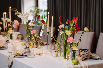 Festive dinner table is served dishes and cutlery and decorated with flowers tulips, greenery,...