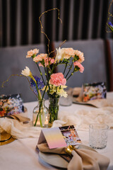 Festive dinner table is served dishes and cutlery and decorated with flowers tulips, greenery, candles. Birthday celebration. Family holidays in modern restaurant. Stylish spring party. Wedding event.