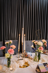 Festive dinner table is served dishes and cutlery and decorated with flowers tulips, greenery, candles. Birthday celebration. Family holidays in modern restaurant. Stylish spring party. Wedding event.