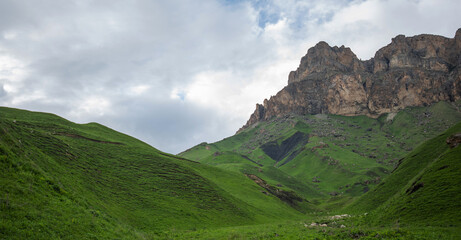 Obraz premium Summer mountain landscape. Amazing view of the valley and lush green pastures in the Caucasus, Georgia. Valley surrounded by high mountain ranges. Cloudy and rainy day in spring, low storm clouds.