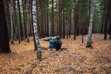 Unrecognizable couple sitting embraced on a large rock on the edge of a mountain and looks at the beautiful landscape of rivers and mountains. Hiking in forest. Tourist couple walking by forest.