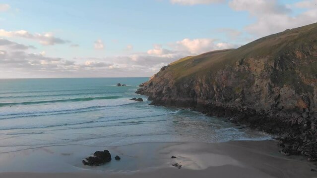 The stunning aerial shot of Perran Sands during sunset, surfers are in the water waiting to catch a perfect wave