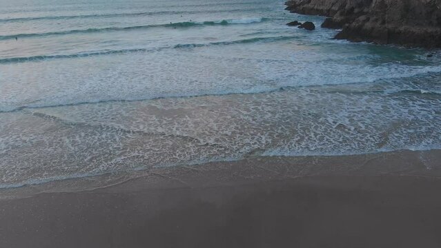 The stunning aerial shot of Perran Sands during sunset, surfers are in the water waiting to catch a perfect wave