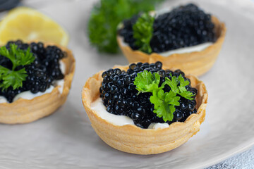 Black caviar in tartlets on a light background. Healthy food concept.