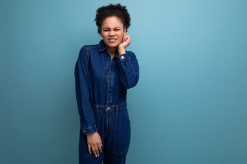 charming slim young hispanic brunette woman with fluffy curly hair in a blue denim suit on a blue background with copy space