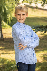 Fototapeta premium Portrait of a little boy in a blue shirt posing in a summer park