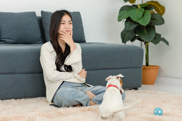 Asian young happy cheerful female owner sit smiling on fluffy carpet floor using toy ball treat training best friend companion dog white short hair jack russell terrier shaking hand in living room