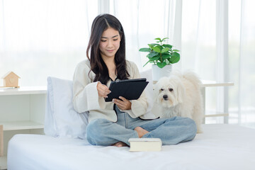 White long hair mutt shih tzu dog laying lying down on bed with Asian young cheerful female owner...