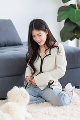 Asian young happy cheerful female owner sitting smiling on fluffy carpet floor playing with best friends companion dogs white short hair shih tzu puppy in living room.