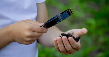 the child holds the earth in his hand and looks through a magnifying glass.