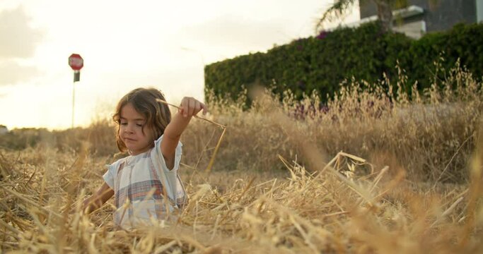 A cute girl dreamily sits on the field and falls into the hay. The concept of a child and nature, working on a farm with a child. High quality 4k footage