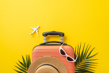 Summer vacation concept. Top view photo of orange suitcase with sunhat and sunglasses on it with palm leaves and plane model on isolated bright yellow background with copyspace