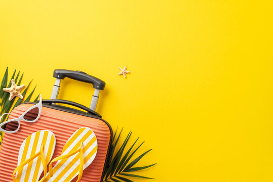 Dream trip concept. Top view photo of orange suitcase with slippers and sunglasses on it with palm leaves and starfish on isolated bright yellow background with copyspace