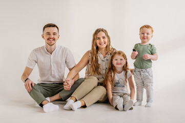 Young happy mother, father with child daughter, son isolated on white background. Funny parents hugs children sit, relaxing on floor near wall at home. Family moving into new house. Relocation concept