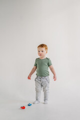 Adorable toddler boy playing with toy car at home, having fun isolated on white background studio, copy space. Child play with colorful toy. Little kid standing on floor in sunny room. Closeup.