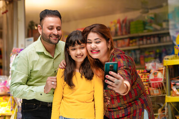 Indian family taking selfie in smartphone at grocery shop.