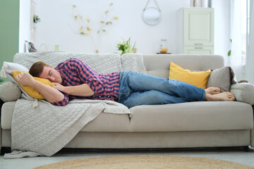 weary man in jeans and shirt succumbs to a nap on his couch, reminding us of the necessity for rest...