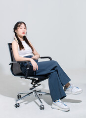 Portrait isolated cutout studio shot Asian young cute female fashion model with pigtails braids hair in sleeveless crop top sitting on adjustable working chair posing look camera on white background