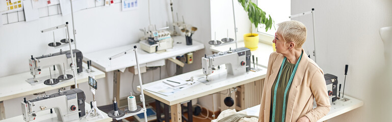Mature dressmaker with stylish short haircut in empty sewing workshop