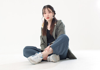 Portrait isolated cutout studio shot Asian young pretty female fashion model with pigtails braids hair in casual plaid suit crop top shirt sitting on floor posing look at camera on white background.