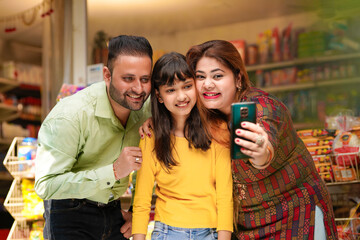 Indian family taking selfie in smartphone at grocery shop.