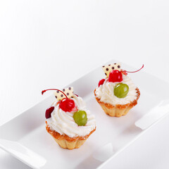 Beautiful cream cakes with cherries and grapes on a plate on a white background