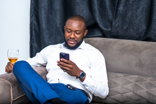 African businessman Happily Relaxes on Sofa While Using Smartphone for Communication