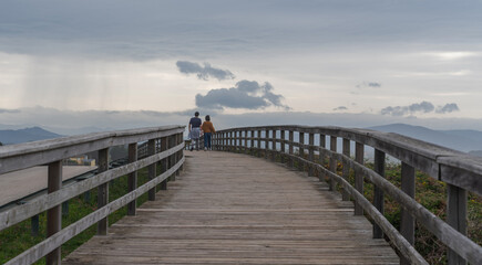 Fototapeta premium A couple in love man and woman walk along a wooden path on the shores of the Atlantic Ocean on a spring evening at sunset on a cloudy day.