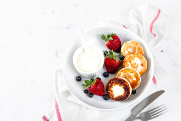 Cottage cheese pancakes, cheesecakes, ricotta fritters with fresh strawberries and blueberries from a white ceramic plate. Healthy and delicious breakfast for the holiday.