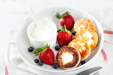 Cottage cheese pancakes, cheesecakes, ricotta fritters with fresh strawberries and blueberries from a white ceramic plate. Healthy and delicious breakfast for the holiday.