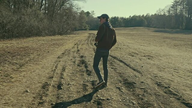 Young photographer walks through an open field in the sunshine (wide)
