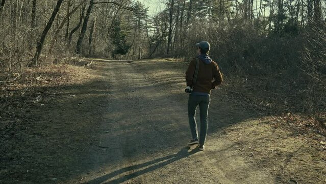 Young photographer walks down a forest trail (wide)