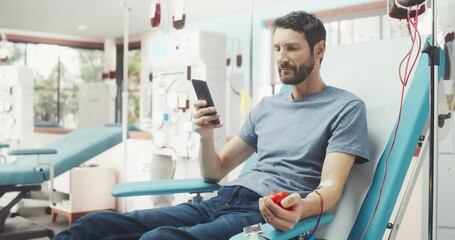 Caucasian Man Donating Blood For People In Need In Hospital. Male Donor Squeezing Heart-Shaped Red Ball To Pump Blood And Chatting Online Using Smartphone. Donation For Victims Of Accidents. - Powered by Adobe