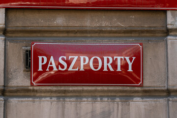 Passport office sign in Poland. Paszporty in Polish means Passports. Red name plate on the wall.