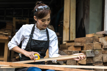 Asian woman Carpenter measures wood with measuring tape in carpentry wood shop, carpenter concept