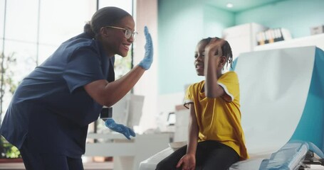 African American Boy Sitting In The Chair In Bright Hospital. Female Black Nurse Putting Patch On A Kid After Polio Vaccine Injection. Professional Woman High-Five Young Man For Not Being Scared.