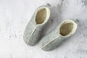 Grey felt wool home winter pair cozy slippers on stone floor background.