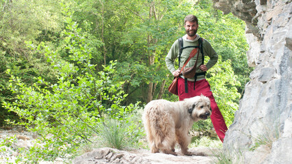 Hombre barbudo y perro recorriendo monte rocoso