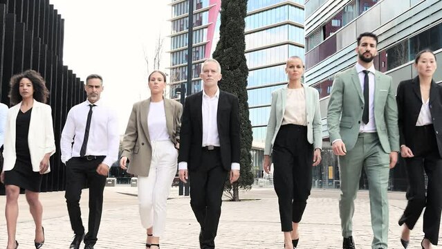 Group of confident business people walking the street together looking at camera. Diverse team of successful businesswoman and businessman walking outside.