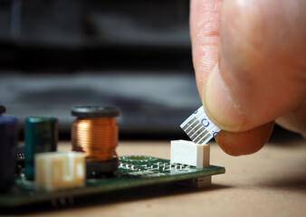 Technician plugging 6-pin flexible flat ribbon cable to the connector on electronic circuit board.
