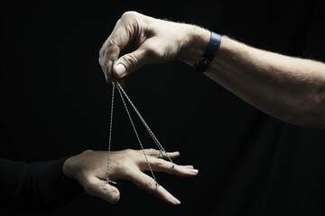 The fingers of a woman's hand are tied with a string. A man's hand holds strings. Dark background.