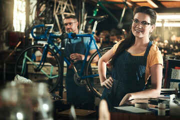 Fototapeta na wymiar Portrait, working and smile of woman in bicycle shop, repair store or cycling workshop. Face, bike mechanic and confident person, professional or technician standing with glasses in small business.