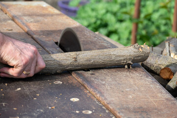 Hands of a worker sawing firewood with an industrial electric circular saw close-up. Harvesting...