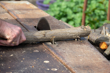 Hands of a worker sawing firewood with an industrial electric circular saw close-up. Harvesting firewood for the winter, sawmill. Sawing firewood with circular saw blade