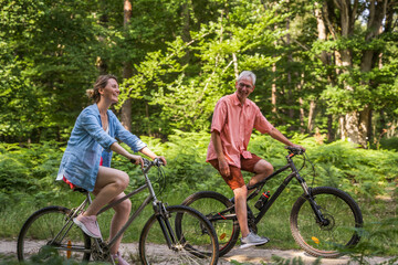 Happy senior father riding bicycles with his daughter through the path in green forest - Powered by Adobe