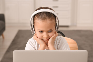 Little girl in headphones using laptop at home. Internet addiction